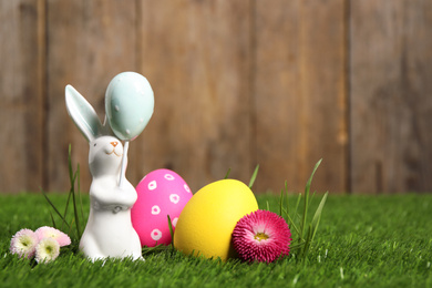 Photo of Colorful Easter eggs, rabbit and daisy flowers on green grass. Space for text