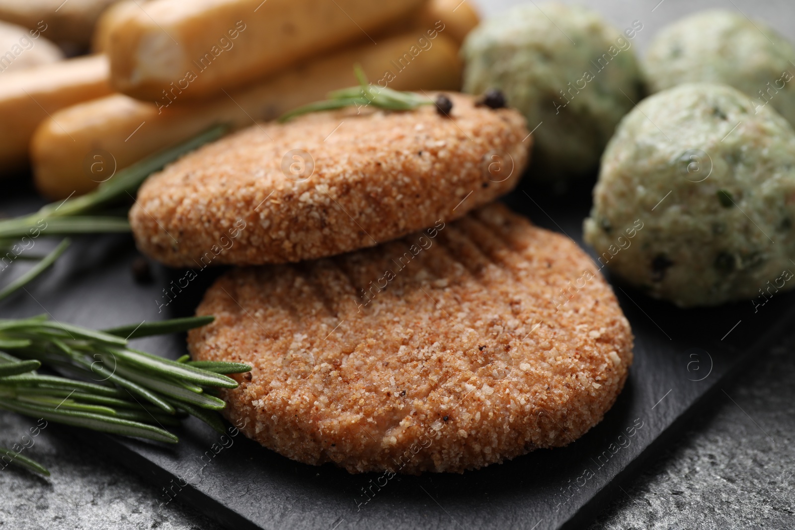 Photo of Raw vegan cutlets and different meatless products on dark board, closeup