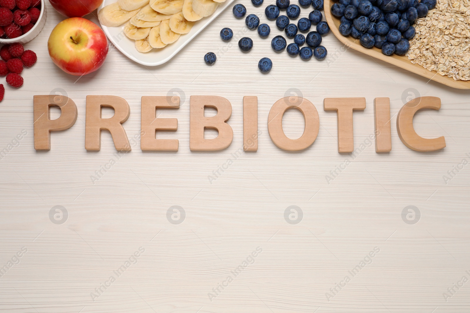 Photo of Word Prebiotic made of letters and foodstuff on white wooden table, flat lay. Space for text
