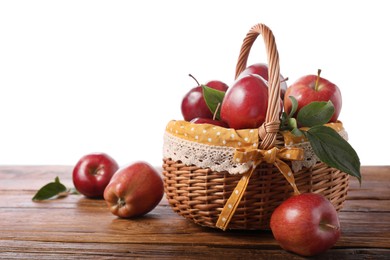 Photo of Ripe red apples in wicker basket on wooden table against white background