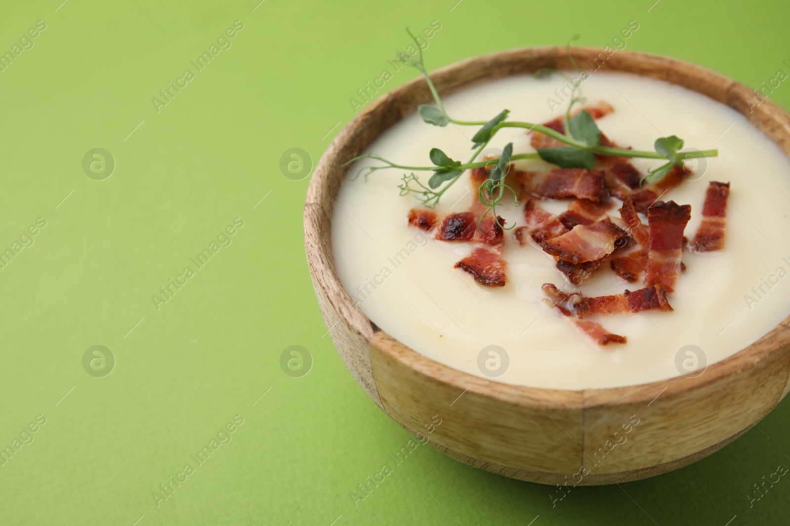 Photo of Delicious potato soup with bacon and microgreens in bowl on green table, closeup. Space for text