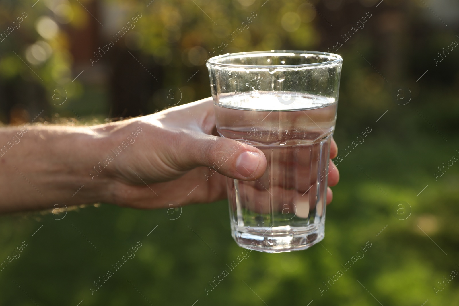 Photo of Man holding glass of fresh water outdoors, closeup