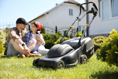 Photo of Happy couple with dog spending time in garden, focus on lawn mower