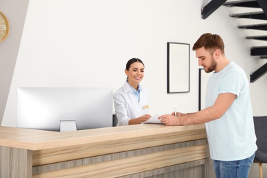 Professional receptionist working with patient at desk in modern clinic