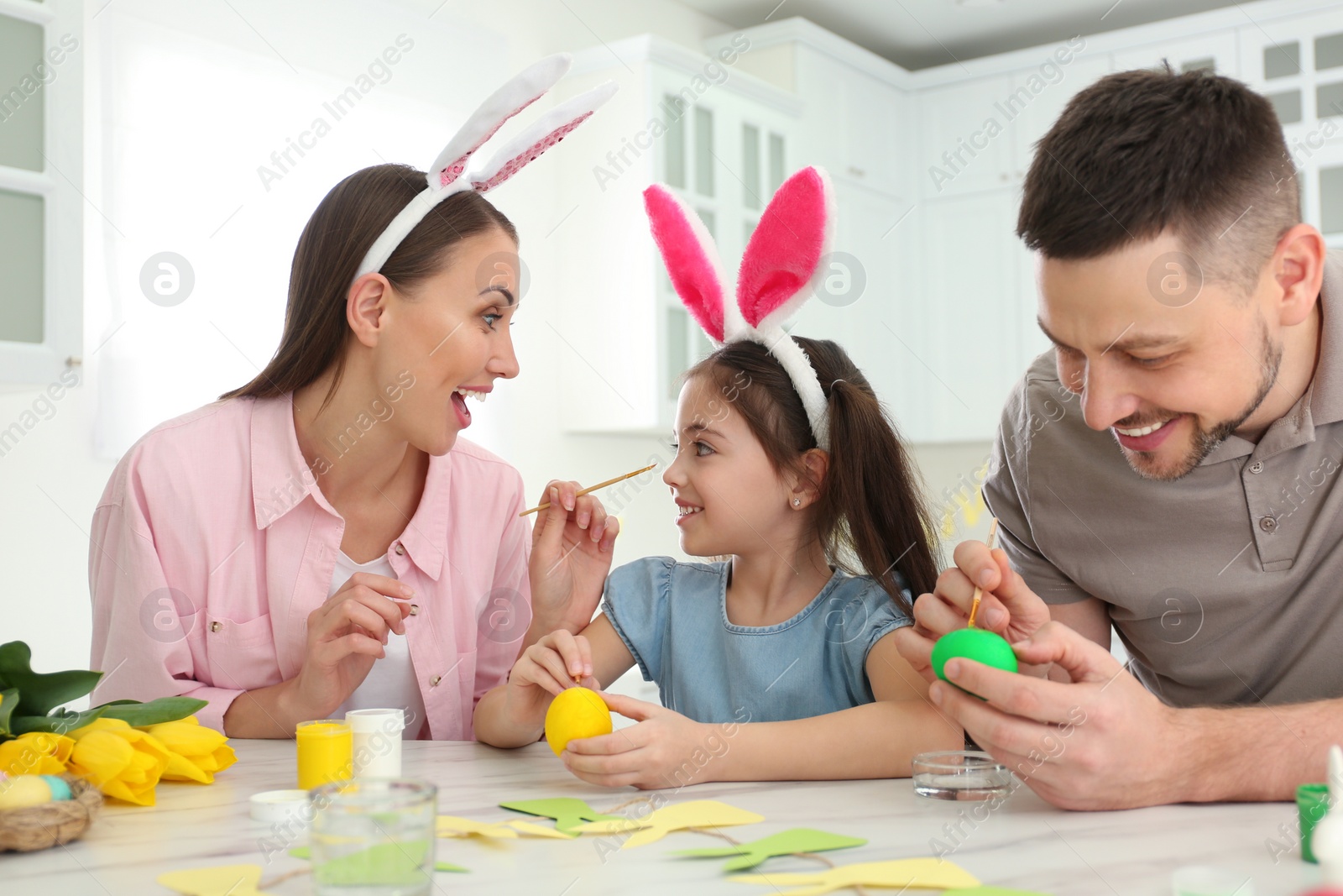 Photo of Happy father, mother and daughter painting Easter eggs at table in kitchen