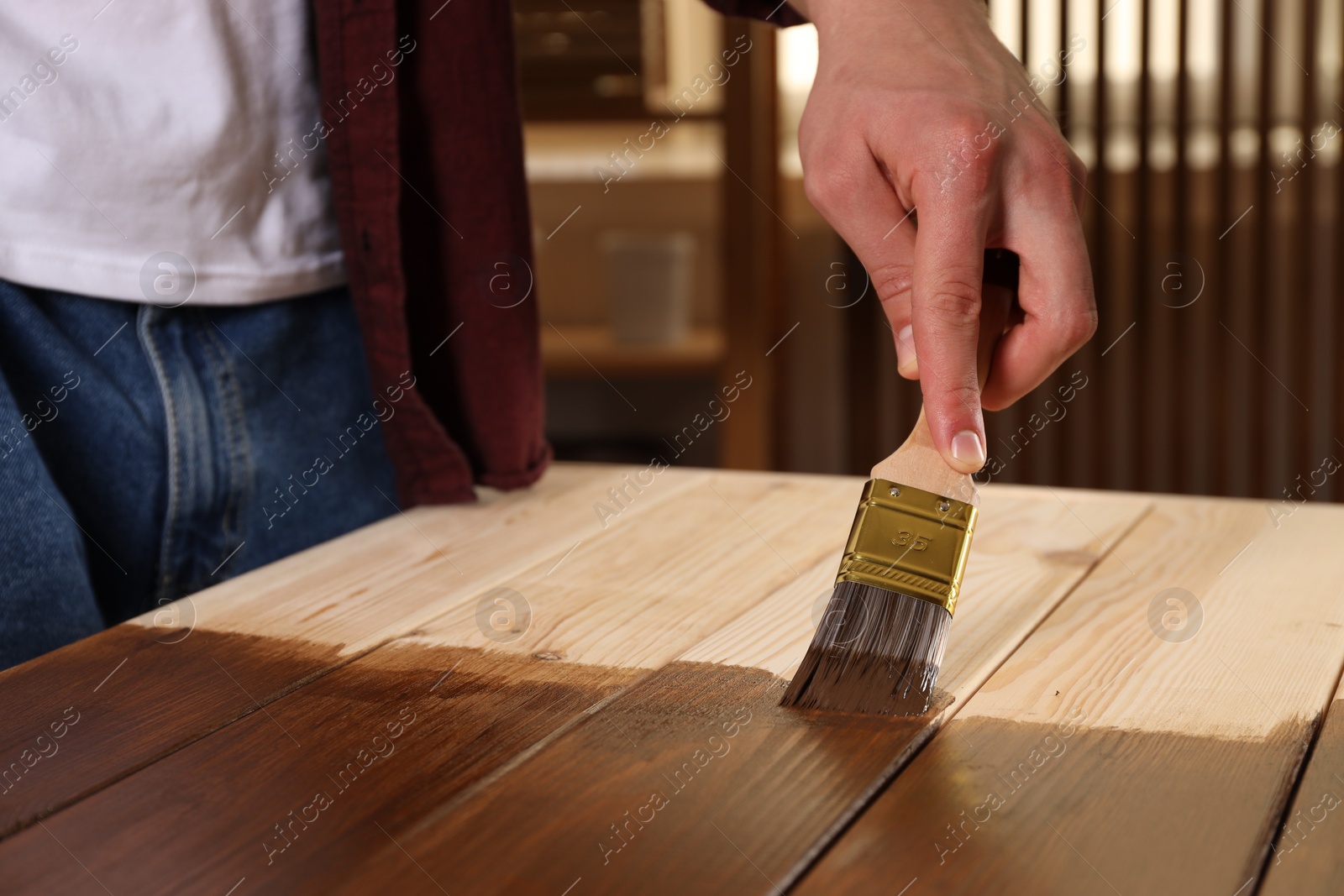 Photo of Man with brush applying wood stain onto wooden surface indoors, closeup