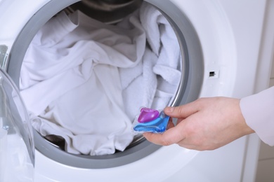 Woman putting laundry detergent capsule into washing machine, closeup