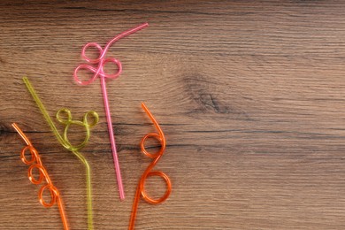 Colorful plastic drinking straws on wooden table, flat lay. Space for text