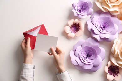 Woman holding envelope with blank greeting card at table, top view