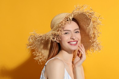 Beautiful young woman in straw hat on orange background, space for text