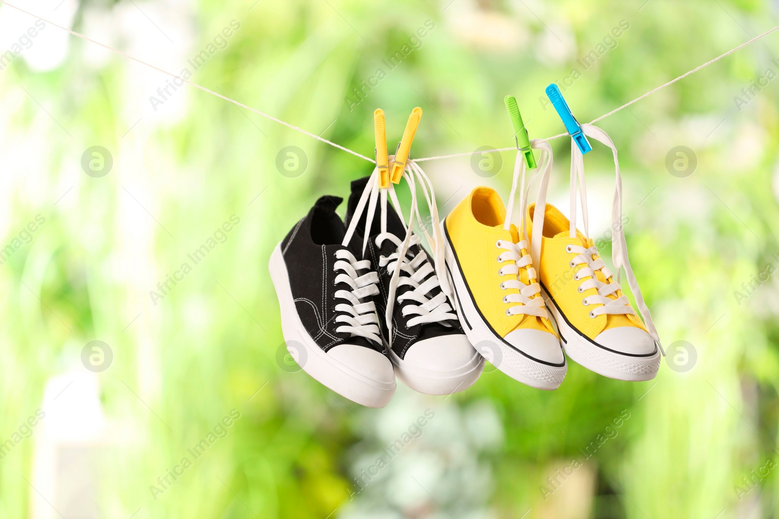 Photo of Different stylish sneakers drying on washing line against blurred background