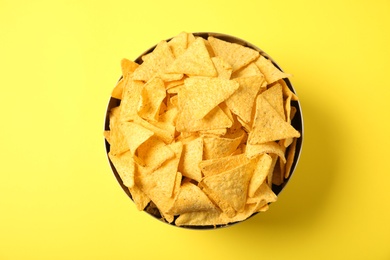 Photo of Tasty mexican nachos chips in metal bowl on yellow background, top view