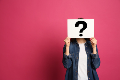 Photo of Woman holding question mark sign on pink background. Space for text