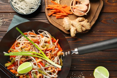 Shrimp stir fry with noodles and vegetables in wok on wooden table, flat lay