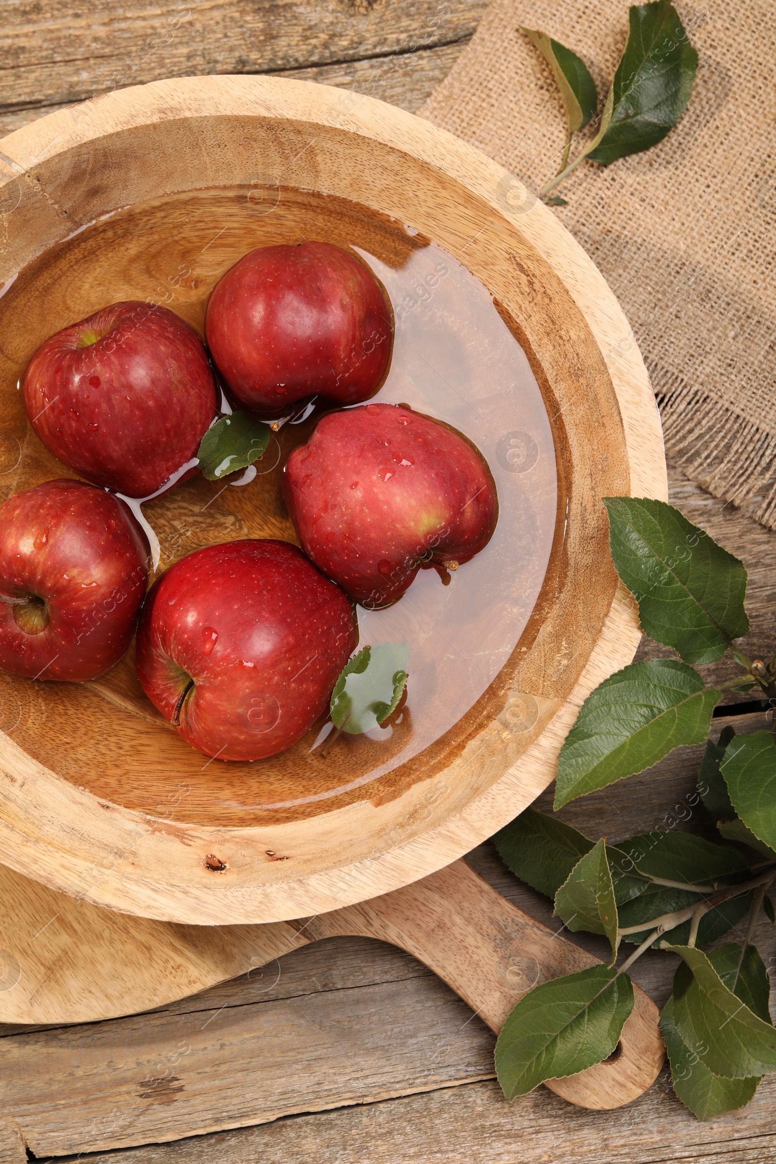 Photo of Fresh red apples in bowl with water and leaves on wooden table, flat lay