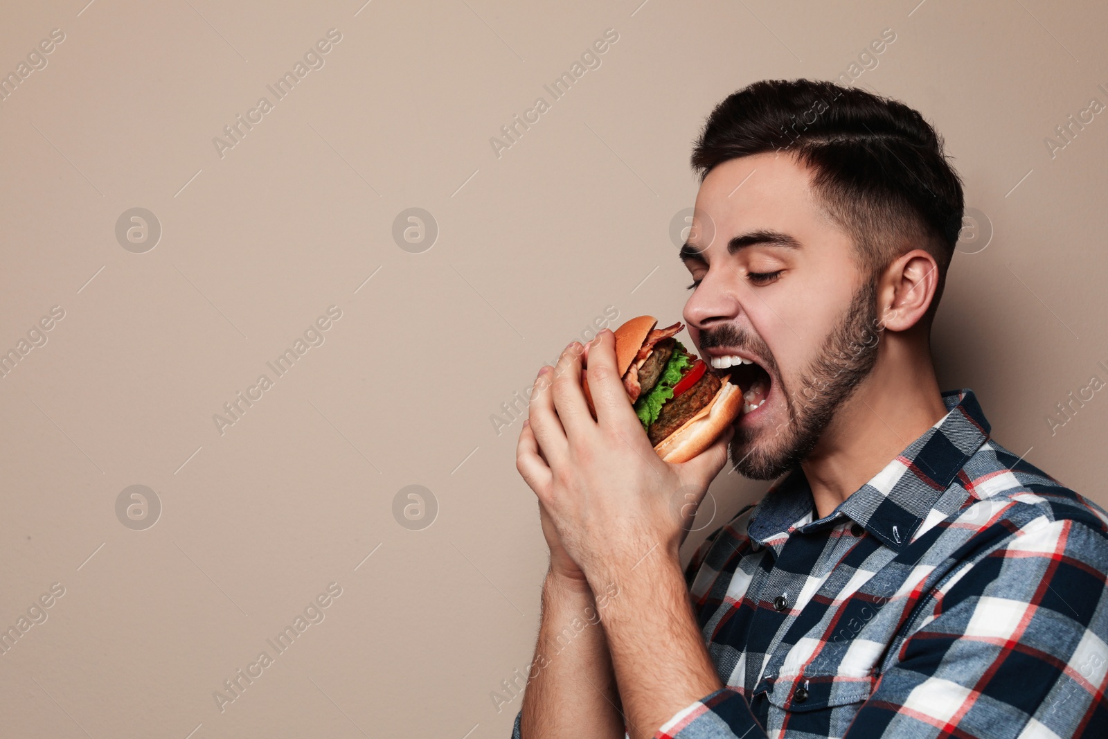 Photo of Handsome man eating tasty burger on color background. Space for text