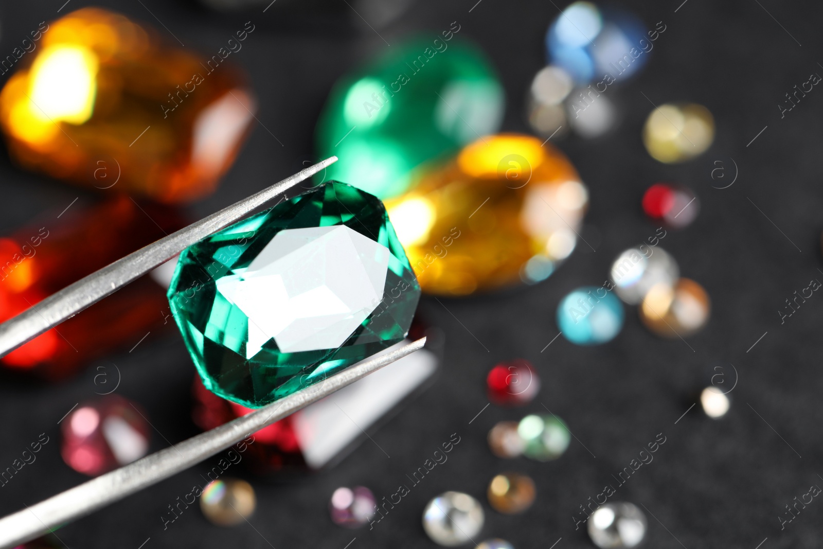 Photo of Tweezers with beautiful gemstone on blurred background, closeup. Space for text