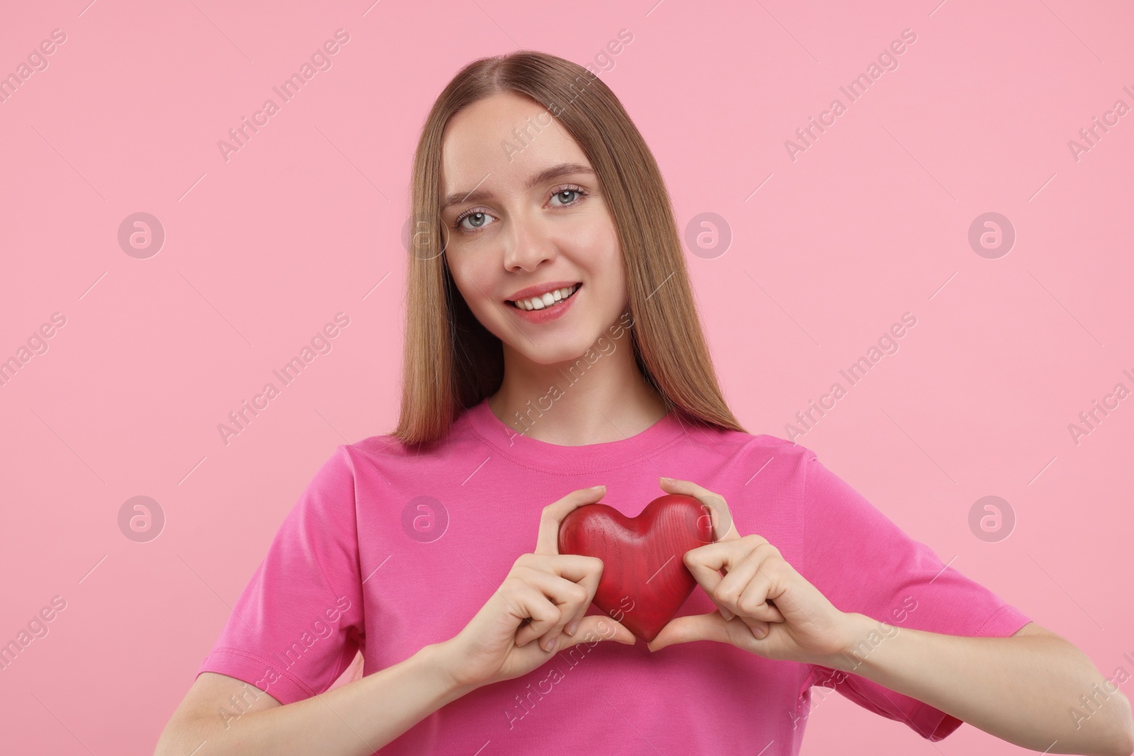 Photo of Happy young woman holding red heart on pink background