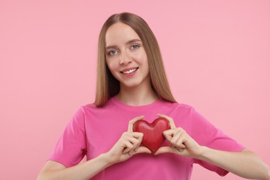 Happy young woman holding red heart on pink background