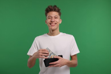 Happy man putting money into his wallet on green background