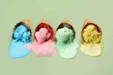 Photo of Melted ice cream in wafer cones on pale green background.