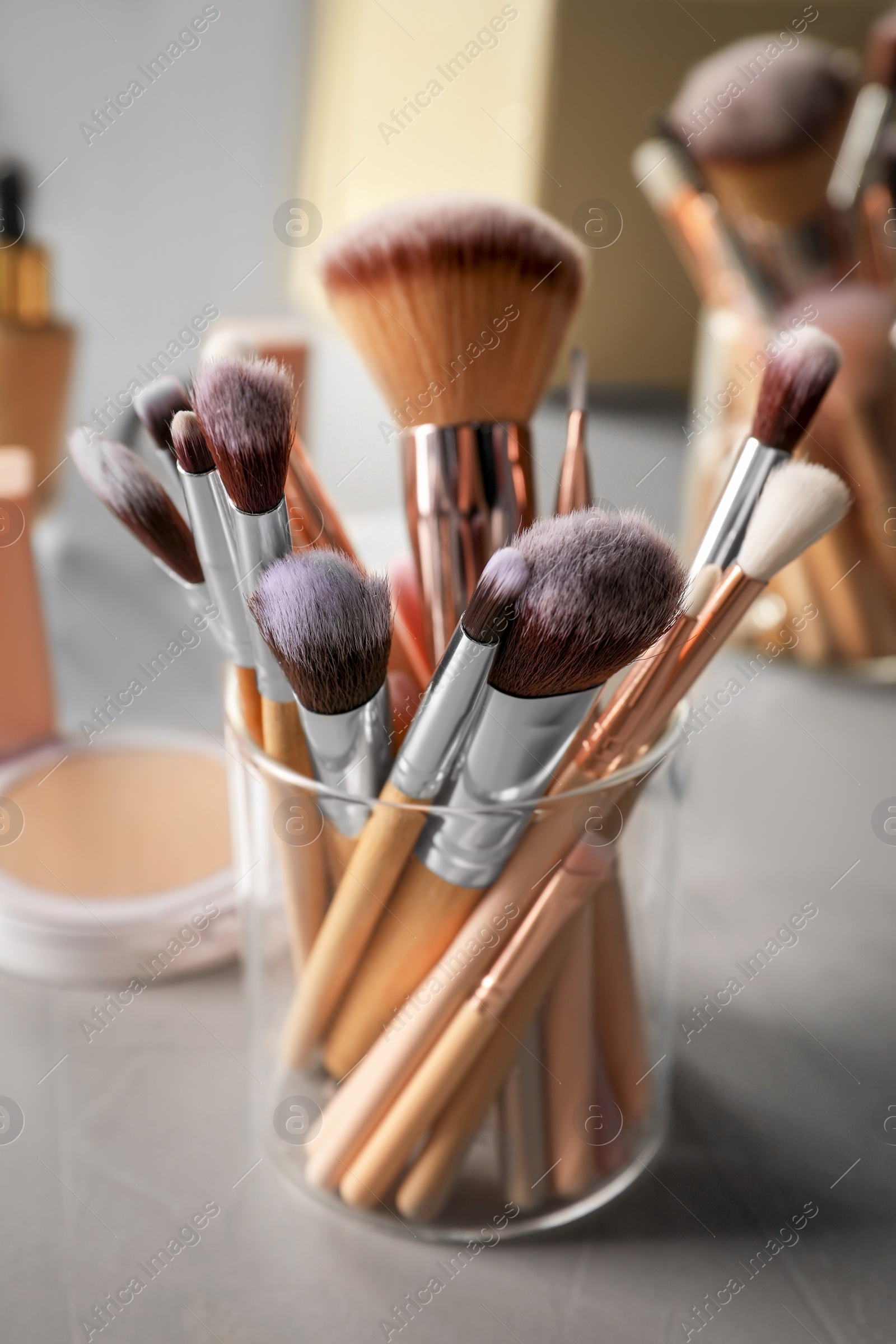 Photo of Set of professional brushes and makeup products near mirror on grey table