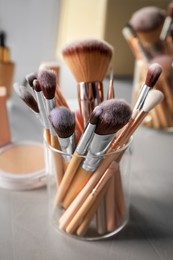 Photo of Set of professional brushes and makeup products near mirror on grey table