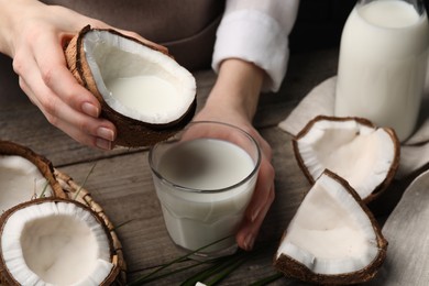 Photo of Woman holding tasty coconut near glass with vegan milk at wooden table, closeup