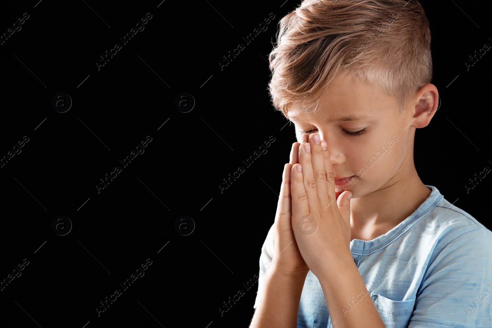 Photo of Little boy with hands clasped together for prayer on black background. Space for text