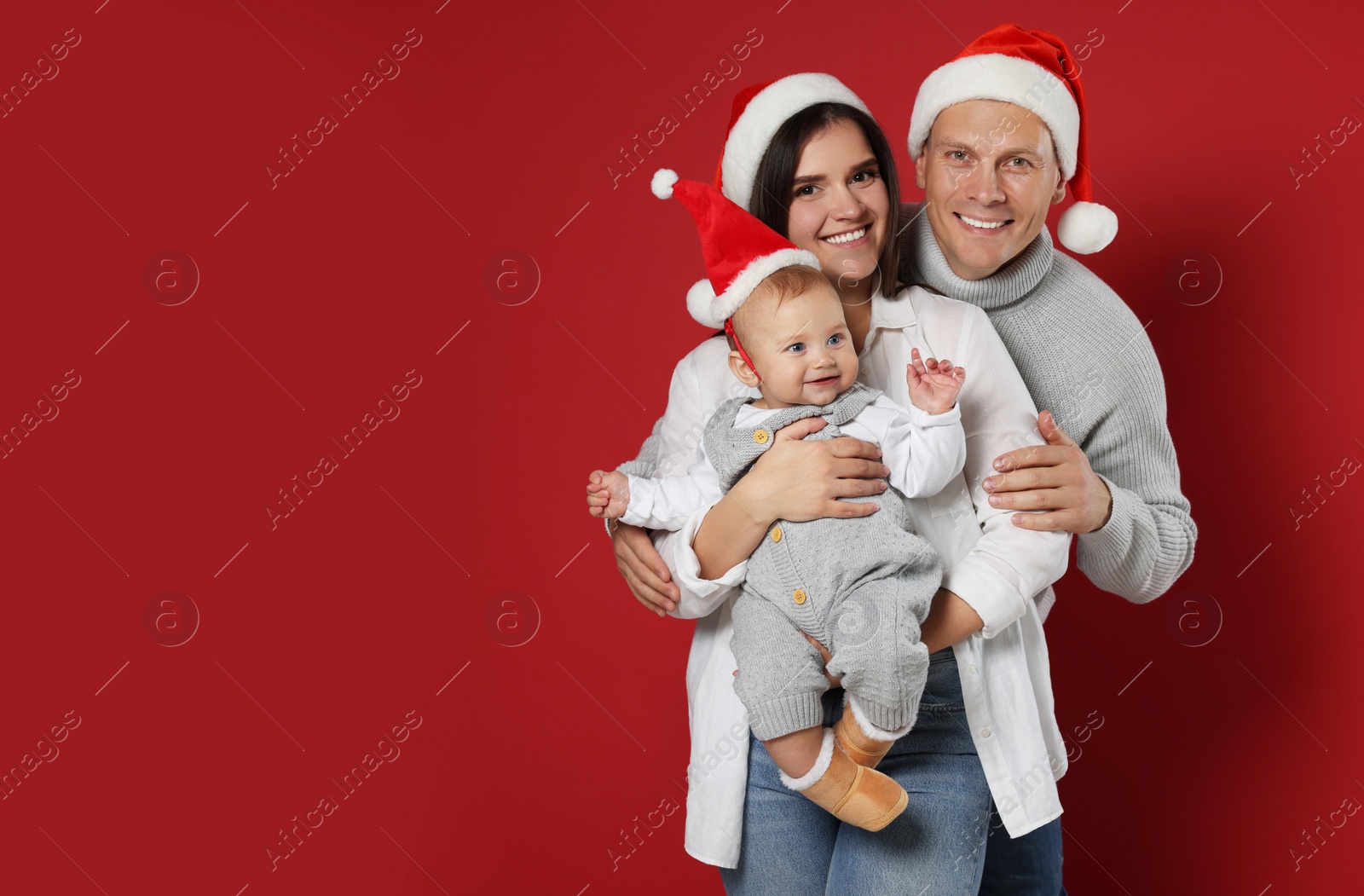 Photo of Happy couple with cute baby wearing Santa hats on red background, space for text. Christmas season