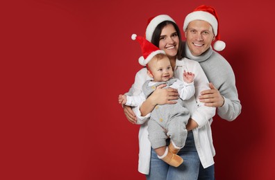 Photo of Happy couple with cute baby wearing Santa hats on red background, space for text. Christmas season