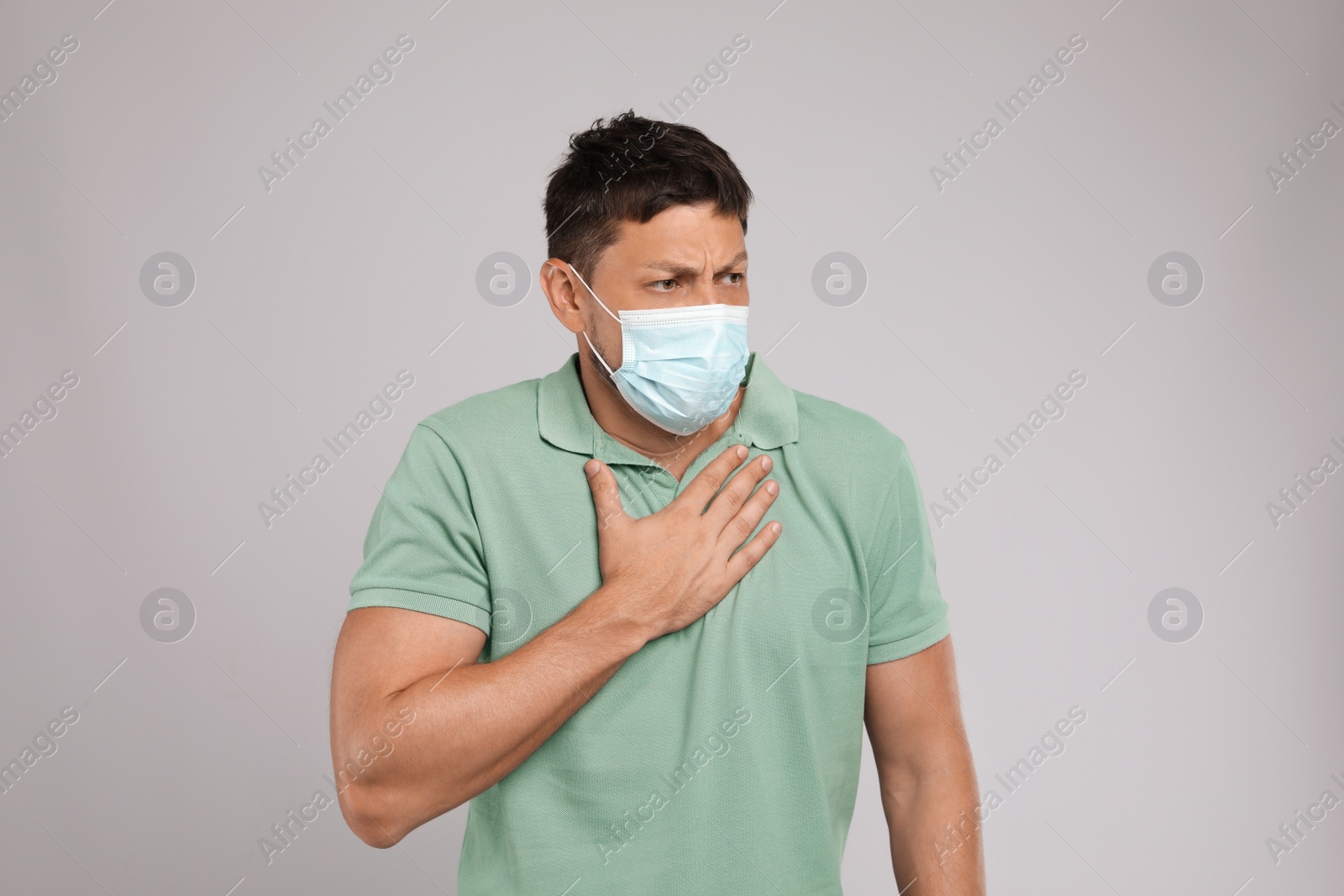 Photo of Man in medical mask suffering from pain during breathing on grey background