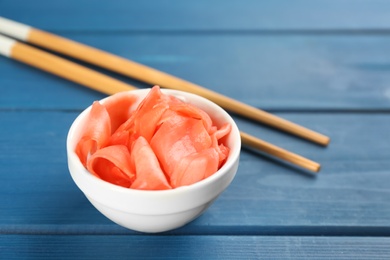 Spicy pickled ginger and chopsticks on blue wooden table, space for text