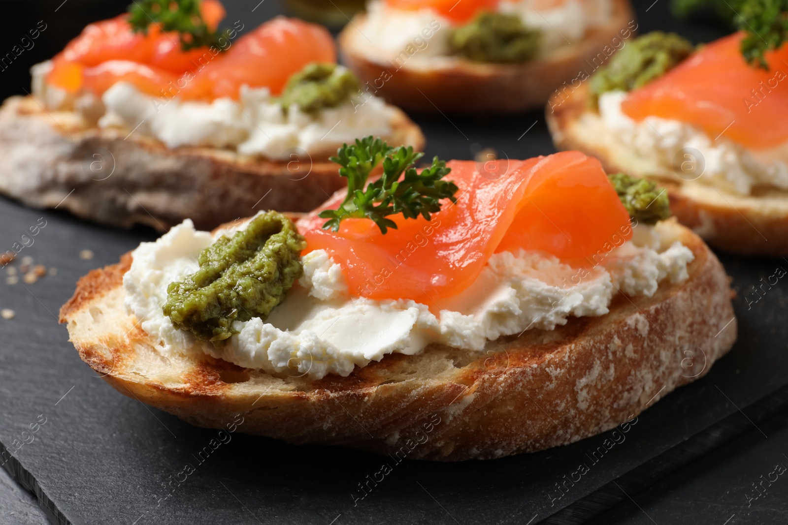 Photo of Delicious bruschettas with cream cheese, salmon and pesto sauce on black table, closeup