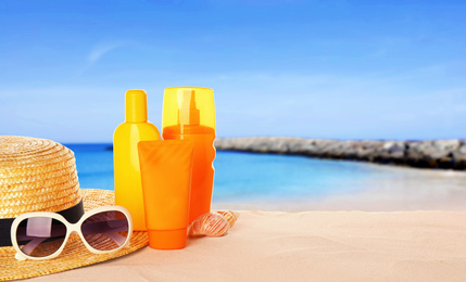 Image of Set of sun protection products and stylish accessories on sandy beach. Space for text