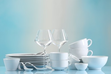 Set of many clean dishware and glasses on light blue table