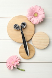 Photo of Metal face roller and flowers on white wooden background, flat lay