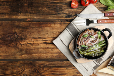Photo of Tasty meat served with asparagus and sprouts in portioned frying pan on wooden table, flat lay. Space for text