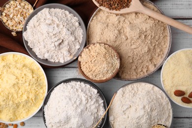 Bowls with different types of flour on white wooden table, flat lay