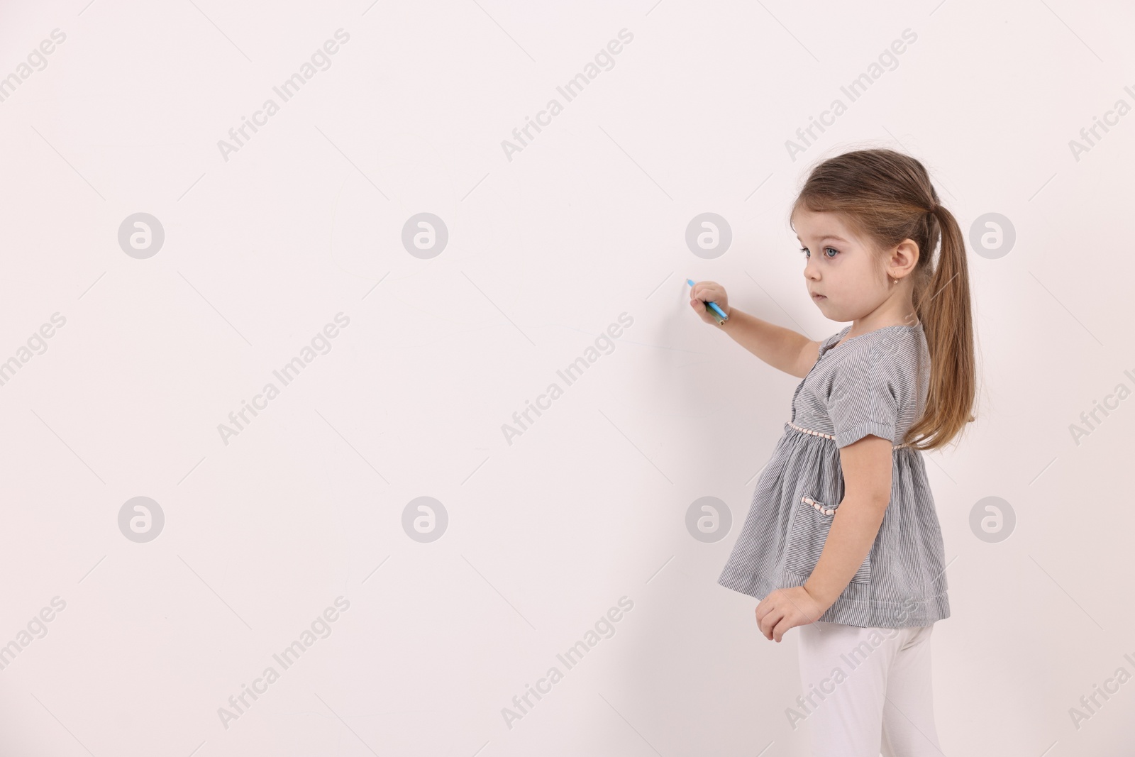 Photo of Little girl drawing with colorful pencils on white wall indoors. Space for text