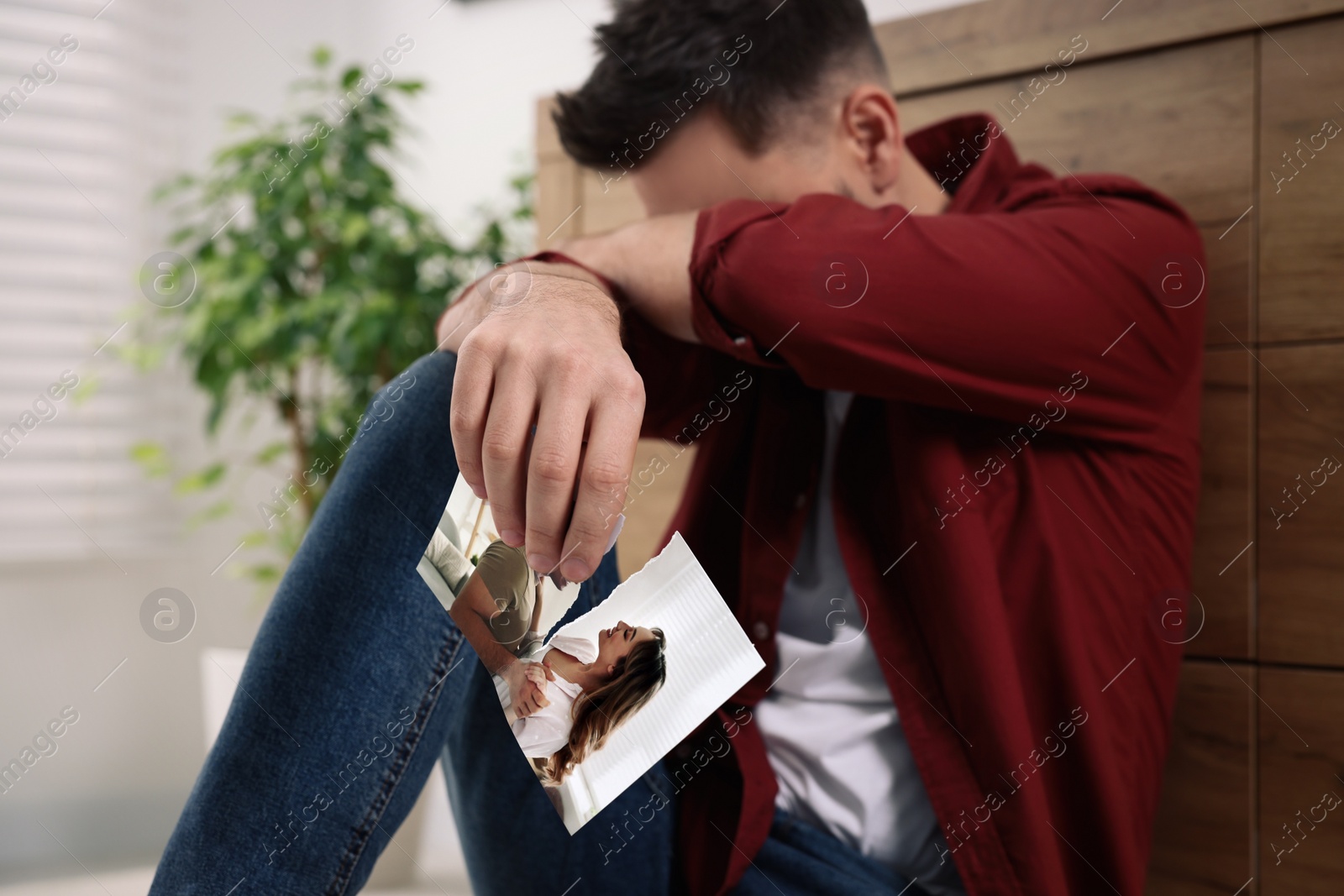 Photo of Crying man sitting on floor indoors, focus on torn photo. Divorce concept
