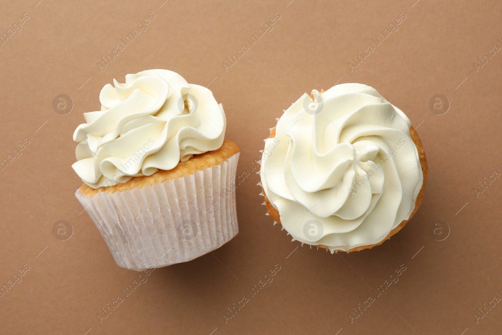 Photo of Tasty vanilla cupcakes with cream on dark beige background, top view