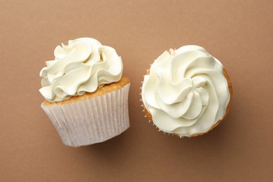 Photo of Tasty vanilla cupcakes with cream on dark beige background, top view