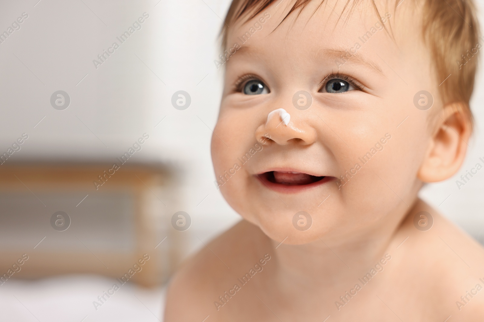 Photo of Cute little baby with moisturizing cream on face indoors, closeup. Space for text