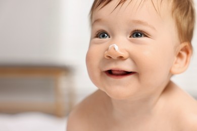 Cute little baby with moisturizing cream on face indoors, closeup. Space for text