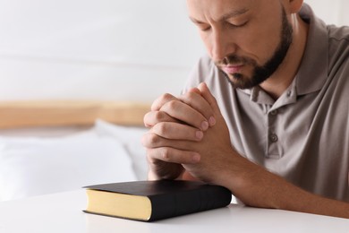 Photo of Religious man with Bible praying in bedroom, closeup