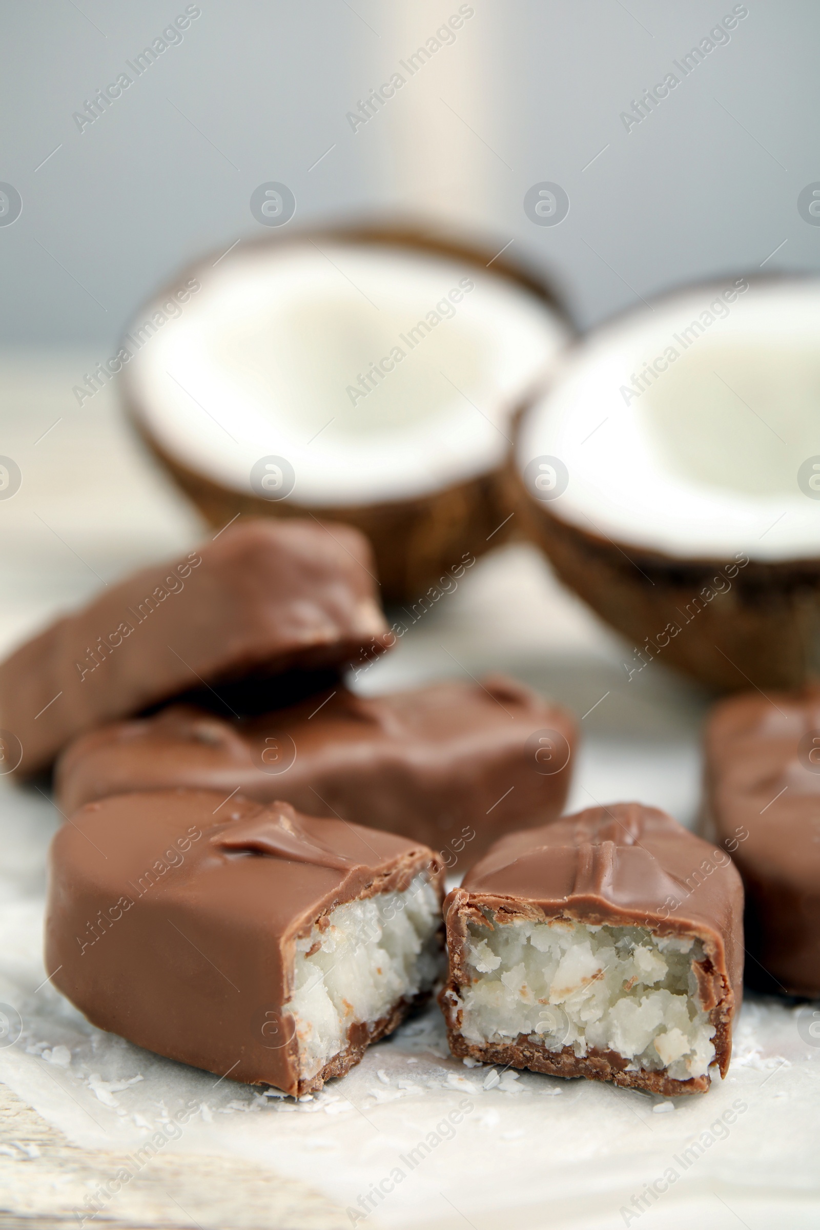 Photo of Delicious milk chocolate candy bars with coconut filling on white table, closeup