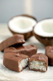 Delicious milk chocolate candy bars with coconut filling on white table, closeup