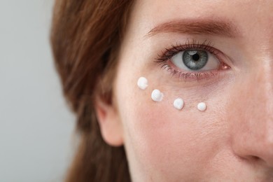 Beautiful woman with freckles and cream on her face against grey background, closeup