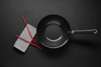 Empty iron wok and chopsticks on black table, flat lay
